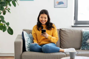 A woman on the couch on her phone participating in a virtual auction.