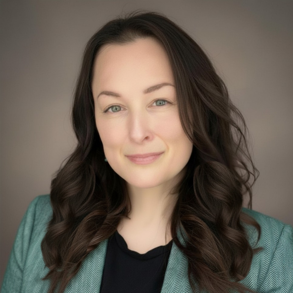 Woman with long dark wavy hair and green eyes wearing a teal blazer over a black top, neutral gray background.